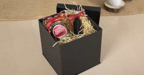 Représentation de la boîte cadeau avec couvercle ouverte et d’exemples de cadeaux comme un pot de pesto et une petite bouteille de vin.